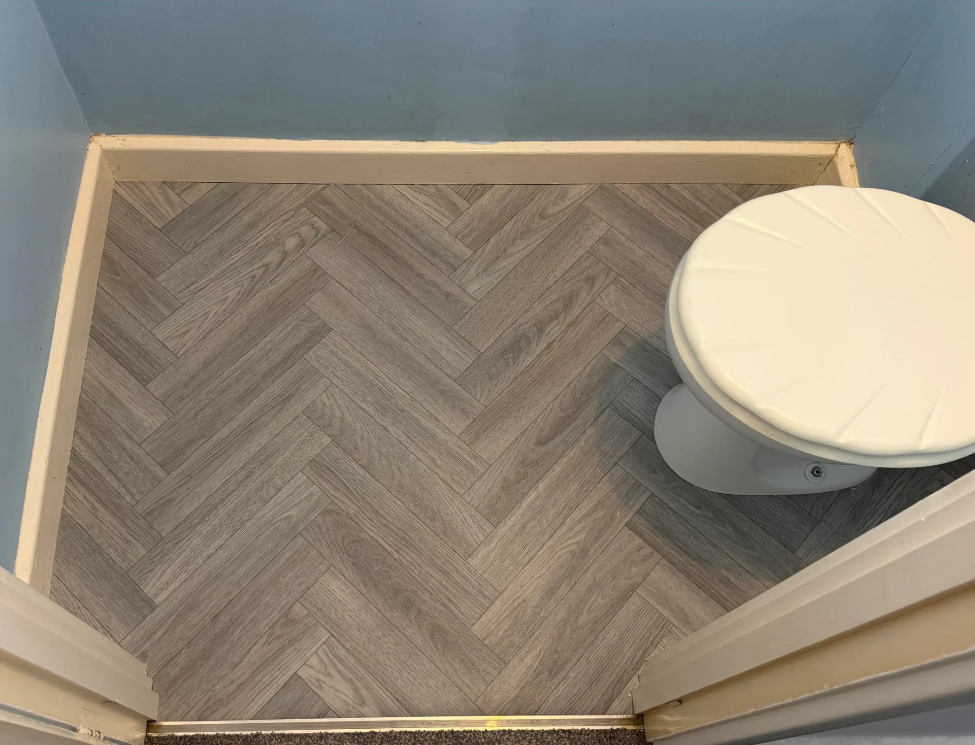 Grey herringbone lino flooring beside a white toilet