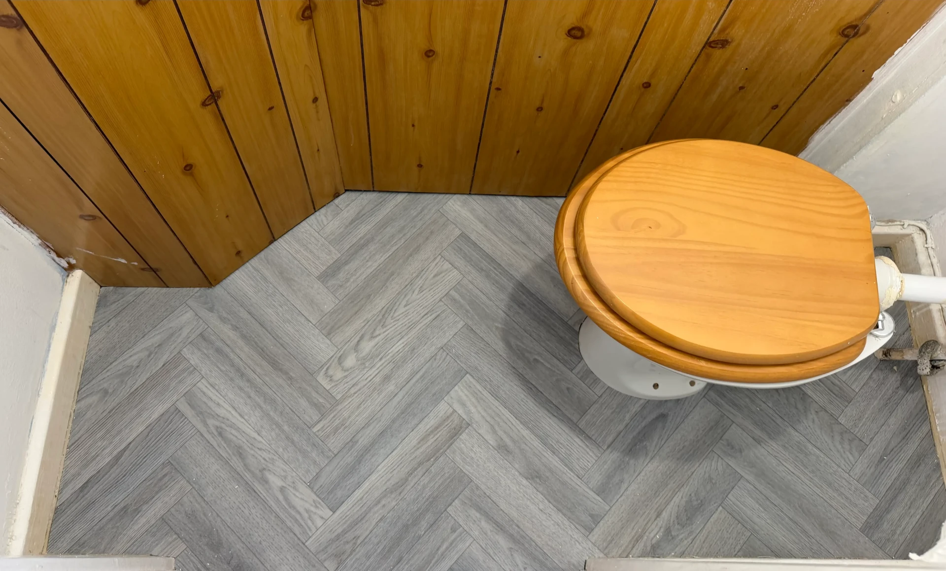 Grey herringbone lino flooring beside a wooden toilet seat
